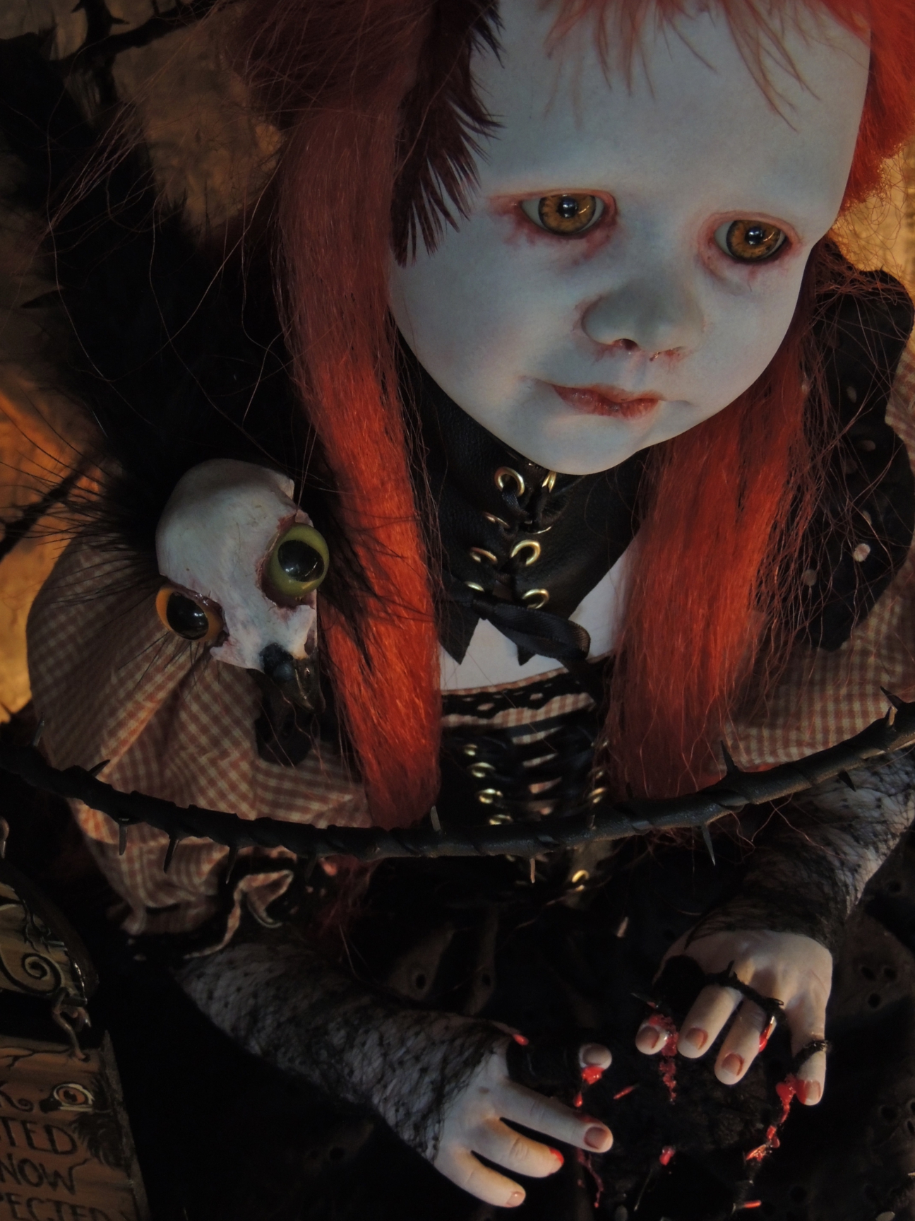close up of red-headed goth doll sitting in a black cage with a skull raven on her shoulder